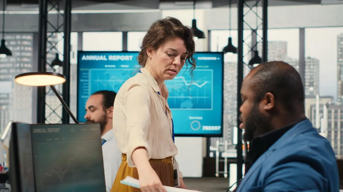 Женщина-секретарь в офисе толкает тележку, нагруженную бумагами.